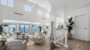 A spacious living area with a large window overlooking the sea, furnished with white sofas and a wooden coffee table.