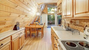 A wooden interior with a kitchen area featuring a dining table, chairs, and a sink.