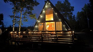 A modern, triangular-shaped cabin with a large glass window, surrounded by trees.