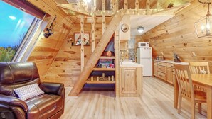 A cozy cabin interior with a wooden staircase, a dining area, and a living room with a leather sofa.