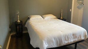 Una cama bien tendida con sábanas blancas, dos mesitas de noche con lámparas y una puerta con perchero.