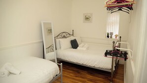 Ein Schlafzimmer mit zwei Einzelbetten, Holzboden, Spiegel und Kleiderständer.