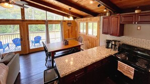 A wooden cabin kitchen with a granite countertop, a stove, and a dining area with chairs and a table. - Pet Friendly Ski House, Game Rm, 4 Mins to Mt Snow (Dover)