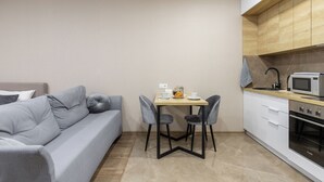A compact living space with a sofa, a small dining table with chairs, a microwave, and a built-in oven. - Apartments in the complex Vogue (Minsk)