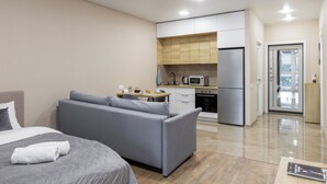 A modern hotel room with a grey sofa, a bed with a white duvet, a small kitchen area with a microwave, and a refrigerator. - Apartments in the complex Vogue (Minsk)