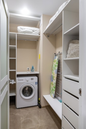 Laundry room with a front-loading washer and drying rack, plus a shelf for folded linens.