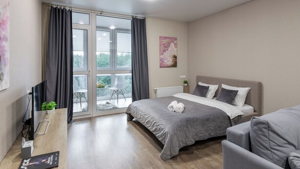 A modern bedroom with a large bed, a desk with a computer, and a view of the outdoors through a sliding glass door. - Apartments in the complex Vogue (Minsk)