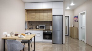 A compact kitchen with a microwave, oven, and refrigerator. There is a dining table with chairs and a small cabinet. - Apartments in the complex Vogue (Minsk)