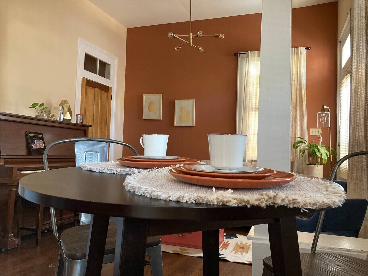 A dining area with a round table set for four, a piano, and framed artwork on the wall.