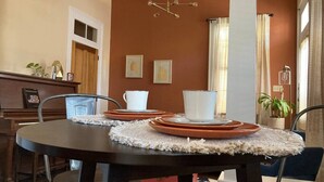 Un coin repas avec une table ronde dressée pour quatre personnes, un piano et des œuvres d’art encadrées accrochées au mur.