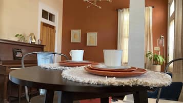 A dining area with a round table set for four, a piano, and framed artwork on the wall.