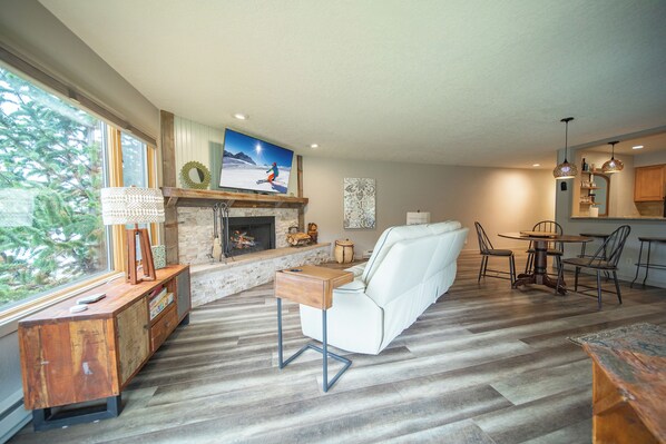 A modern living room with a fireplace, a sofa, and a dining area with a round table and chairs. - Willows 1703 (Keystone)