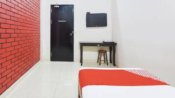 A room with a red brick wall, a black door, a desk with a stool, and a bed with a red and white bedspread.