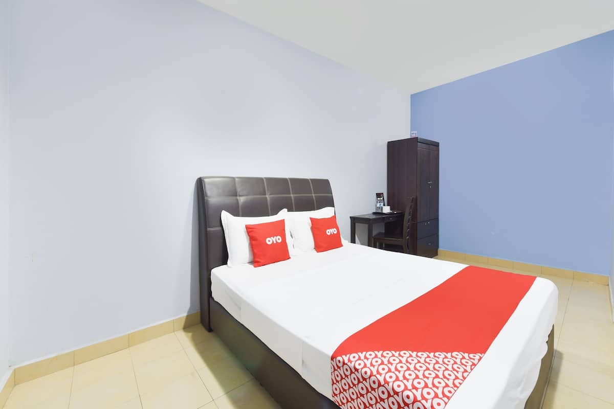 Un lit bien fait, recouvert d’une couvre-lit blanche et rouge, avec une tête de lit sombre et deux oreillers rouges sur lesquels est inscrit le mot « OYO ».