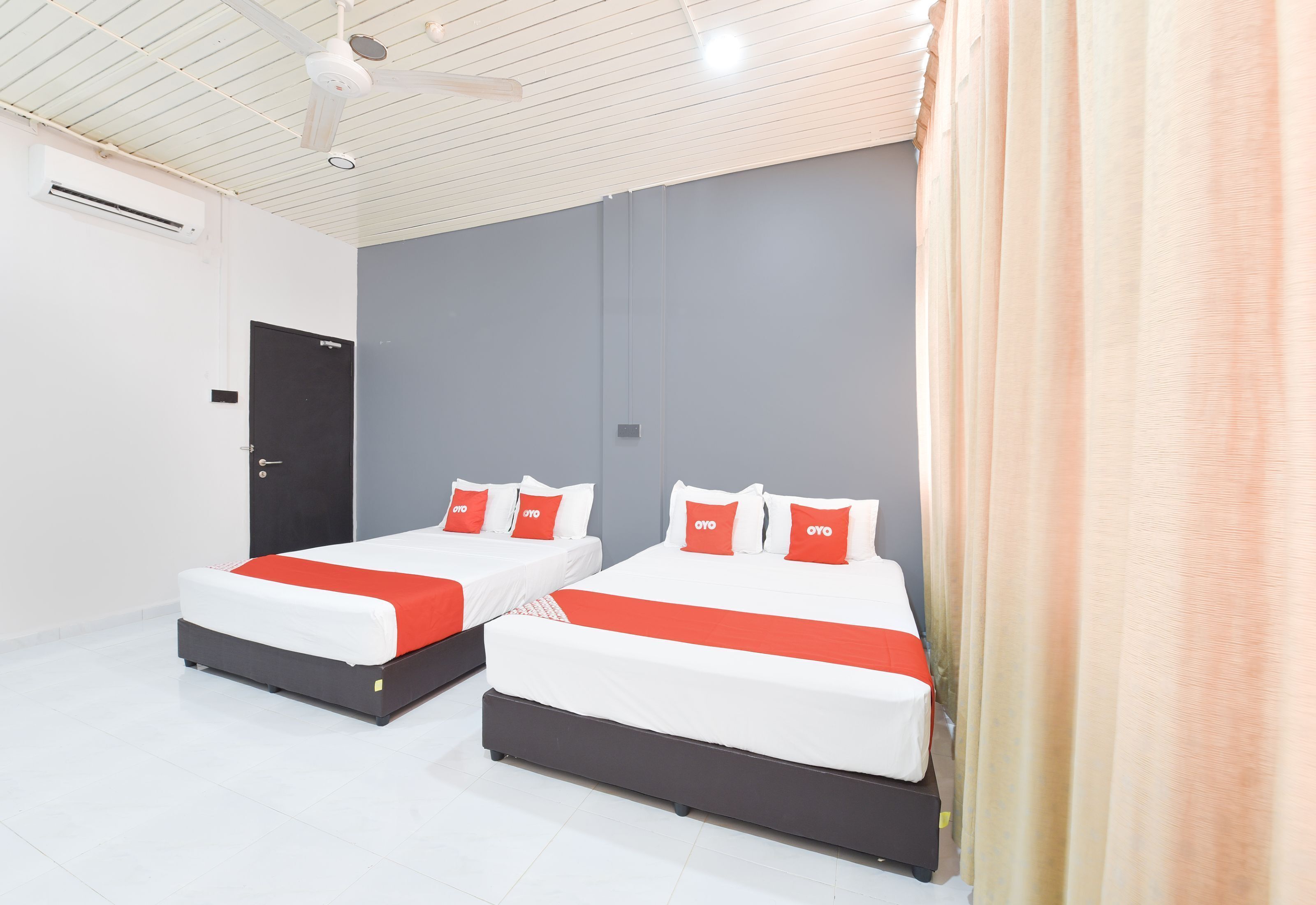 Habitaci ón de hotel con dos camas, cada una con ropa de cama blanca y detalles rojos, un ventilador de techo y una puerta.