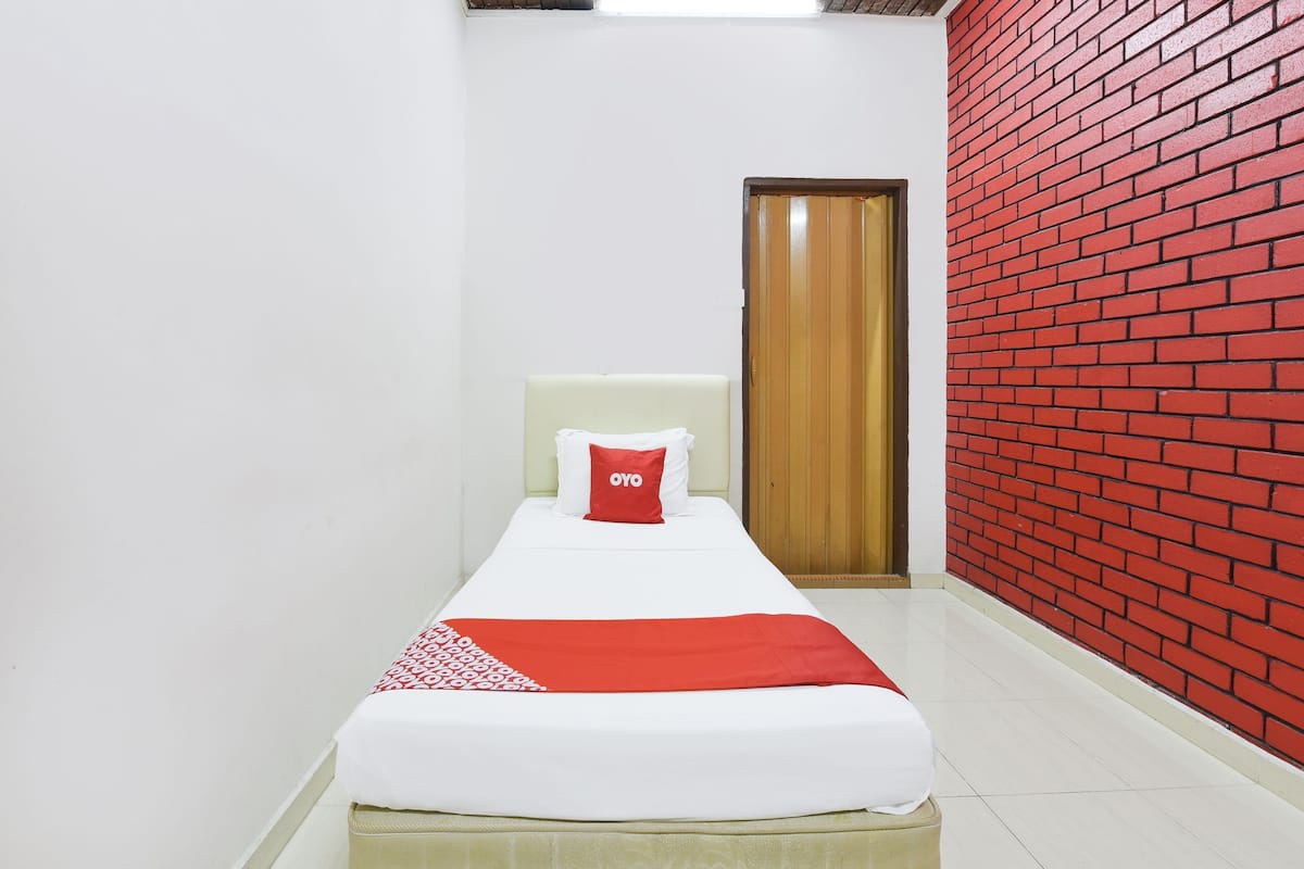 Une chambre avec un lit simple, décorée dans des tons de rouge et de blanc, avec une porte en bois et un mur en briques rouges.