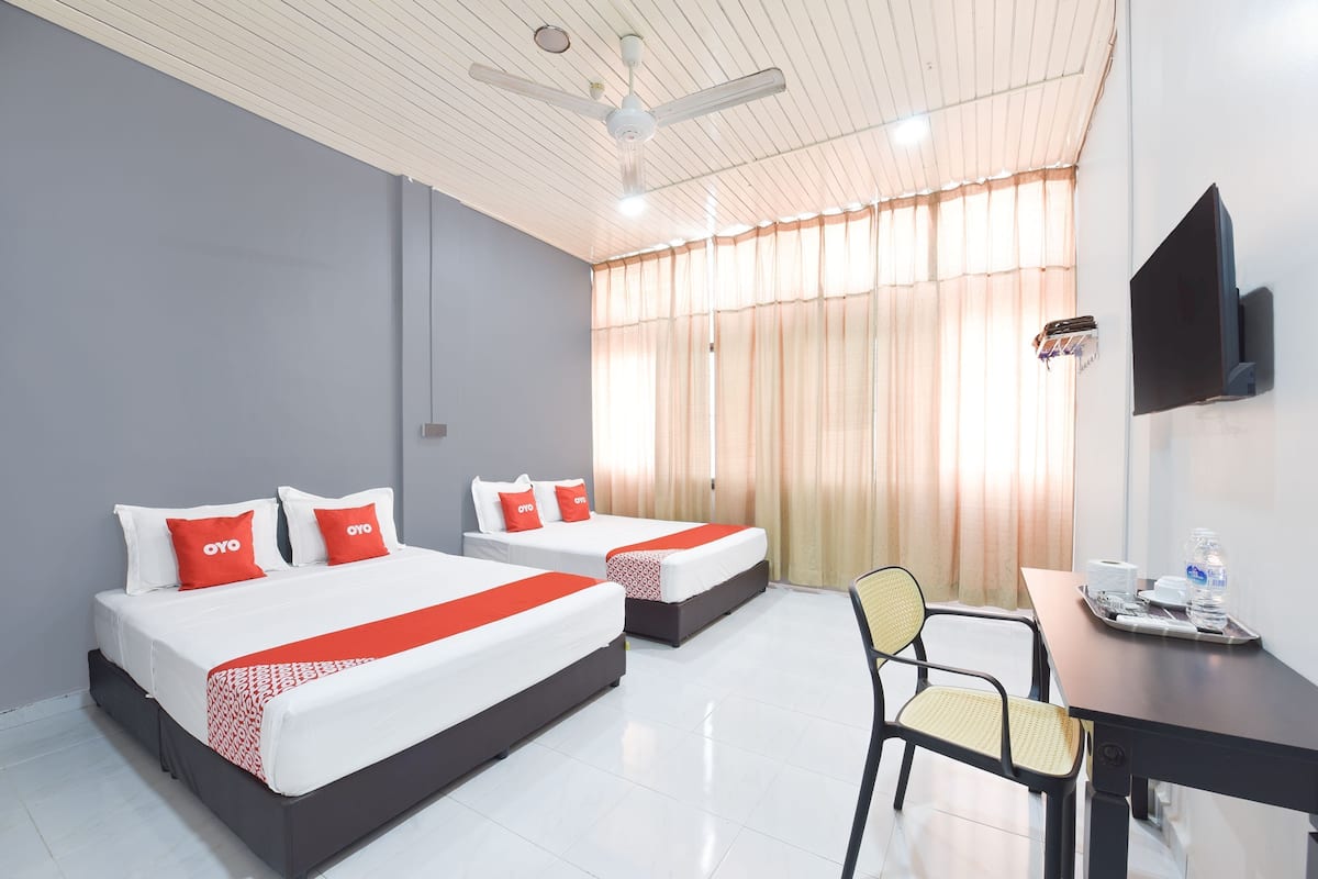 Une chambre d’hôtel avec deux lits, un bureau, une chaise, une télévision et un ventilateur de plafond.