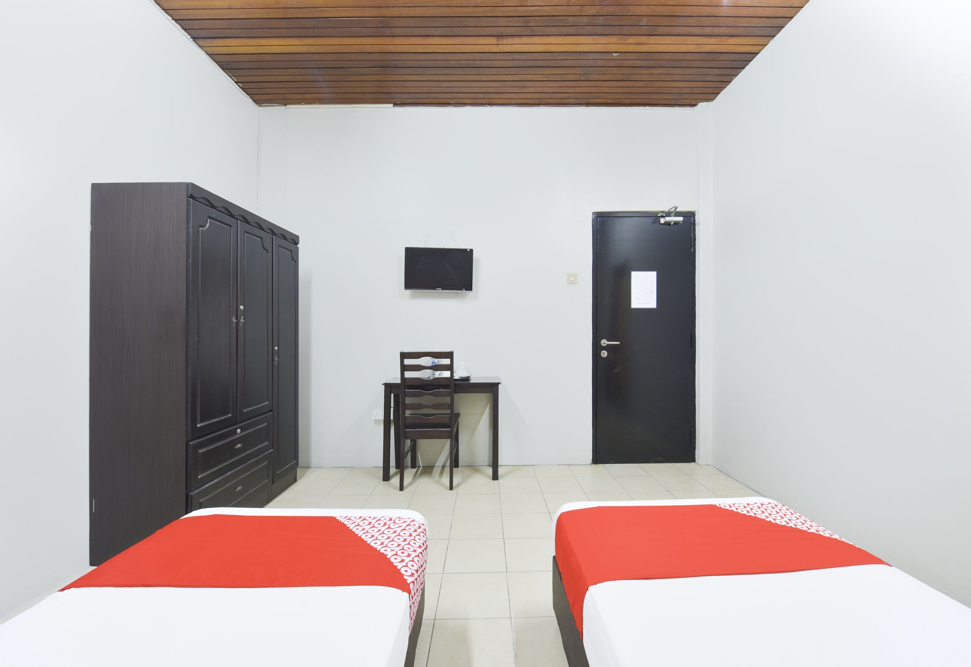 Una habitación con dos camas, un armario, un escritorio con silla, un televisor y una puerta.
