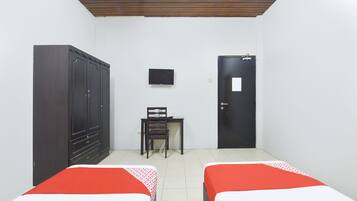 Una habitación con dos camas, un armario, un escritorio con silla, un televisor y una puerta.