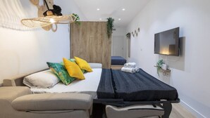 Una habitación de hotel moderna con cama, sofá, televisor y una planta pequeña.