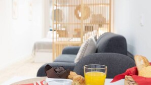 Une table dressée pour le petit-déjeuner avec un verre de jus d’orange, une barre de chocolat et du pain.