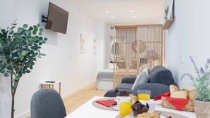 Un salon moderne avec un canapé, une table à manger où sont disposés des aliments pour le petit-déjeuner, un téléviseur fixé au mur et une plante.