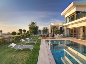 Un área de piscina moderna al aire libre con sillones de descanso, un comedor y vista despejada al océano.