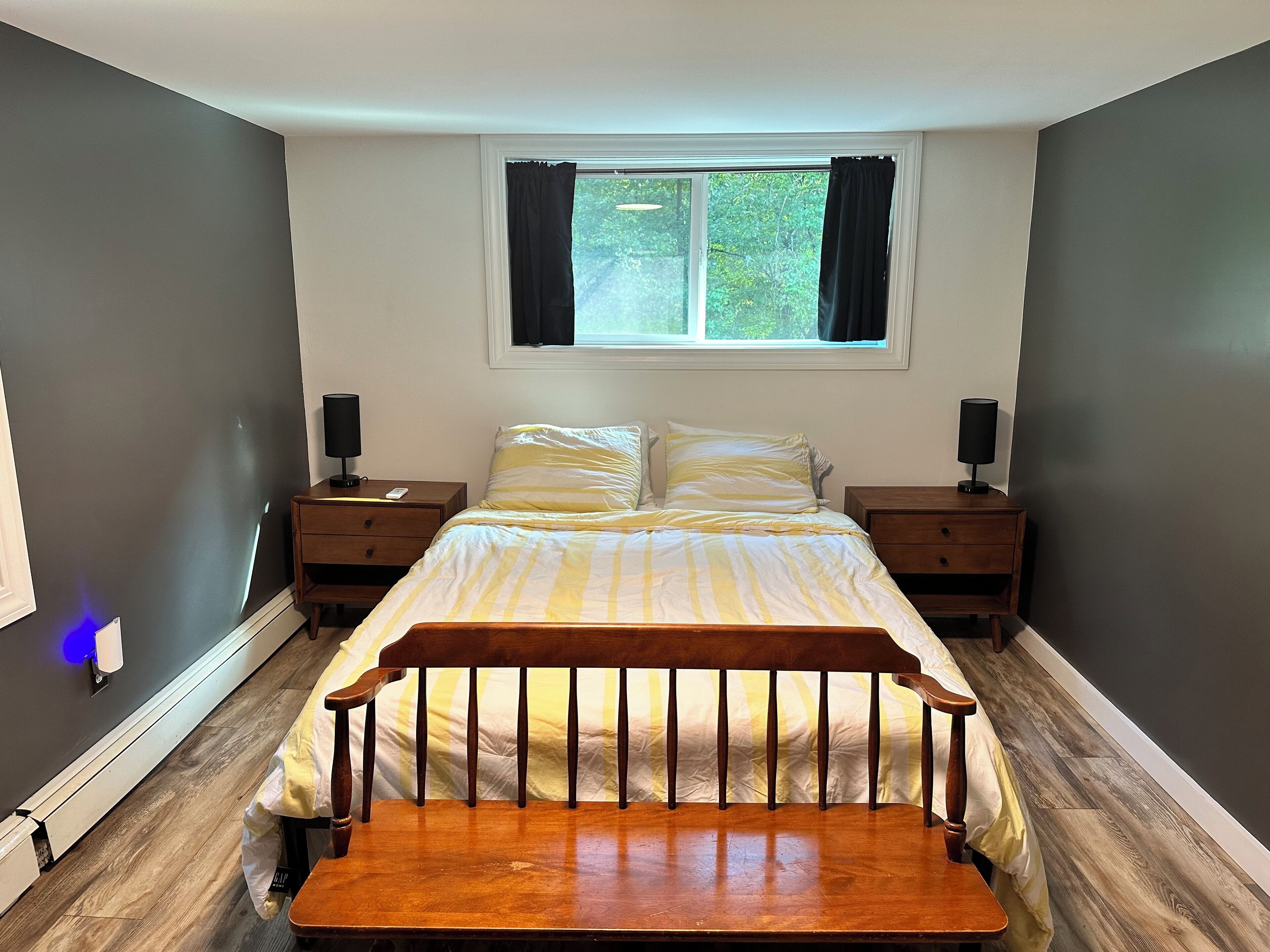A bedroom with a bed, two bedside tables, a window with curtains, and a nightstand with a lamp.
