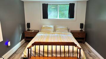 A bedroom with a bed, two bedside tables, a window with curtains, and a nightstand with a lamp.