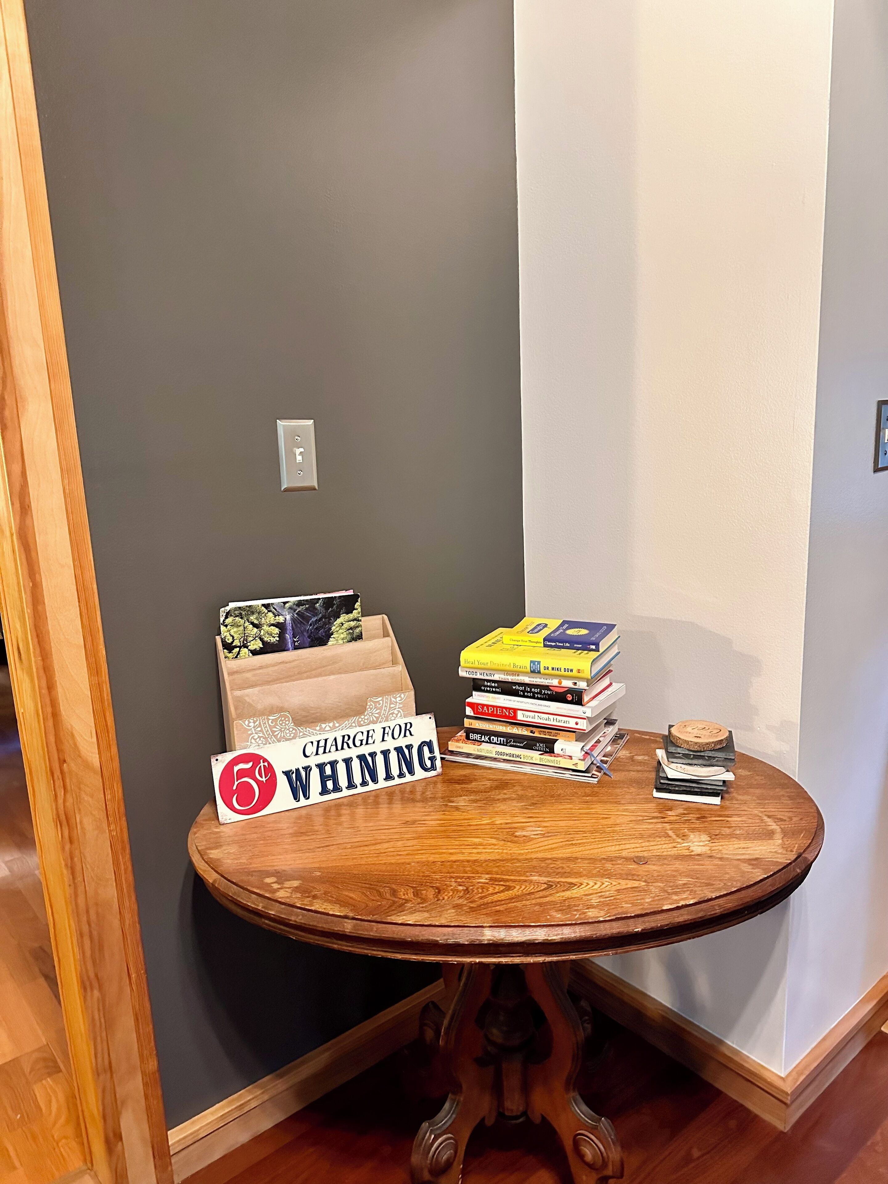 A corner of a room with a wooden table holding books and a sign that reads "CHARGE FOR WHINING".