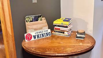 A corner of a room with a wooden table holding books and a sign that reads "CHARGE FOR WHINING".