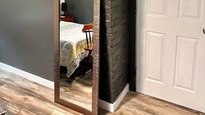 A room with a large mirror, a wooden floor, a dark brick wall, and a white door.