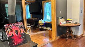 A living room with a fireplace, a painting, a table with books, and a wooden door leading to another room.
