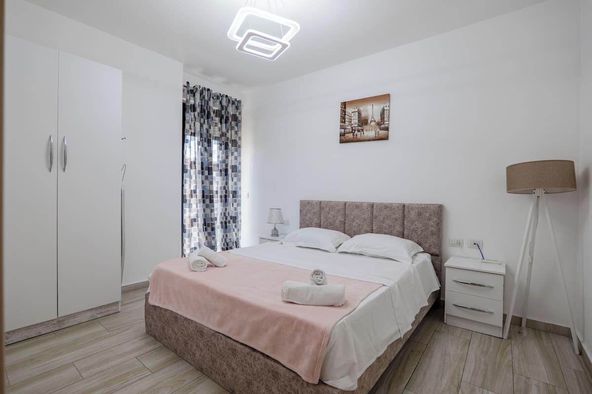 Une chambre à coucher avec un lit, une table de chevet, une lampe, une armoire et un tableau accroché au mur.