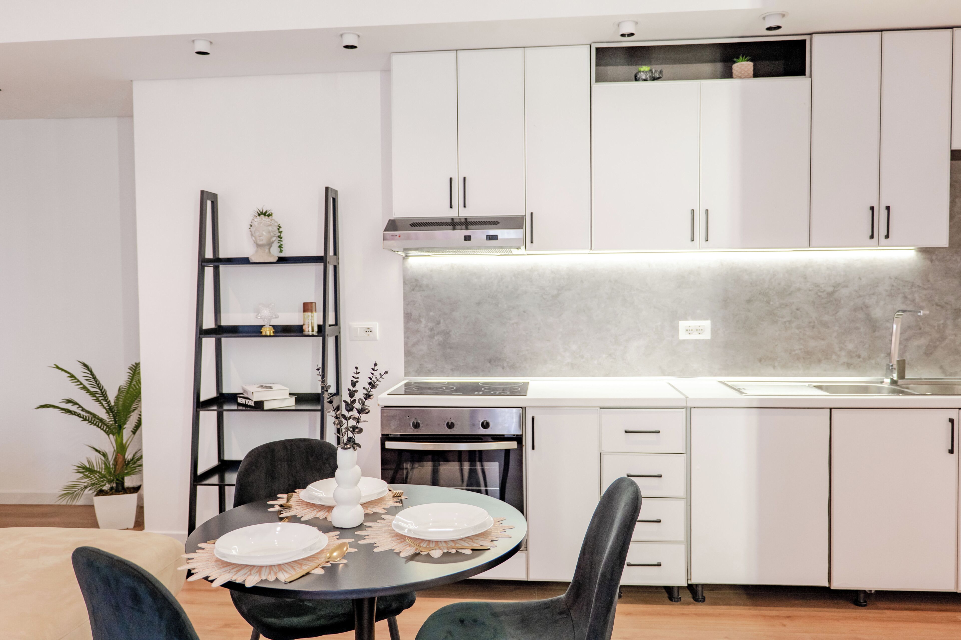 A modern kitchen with white cabinets, a built-in oven, and a dining area with a round table and chairs.