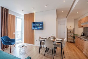 Een moderne woonkamer met een eethoek, een aan de muur bevestigde televisie en een keuken met houten keukenkastjes.