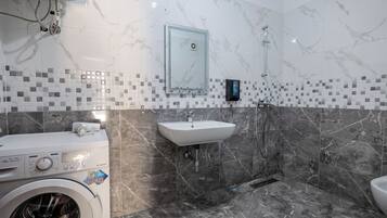 A bathroom with a washing machine, a sink, and a shower.