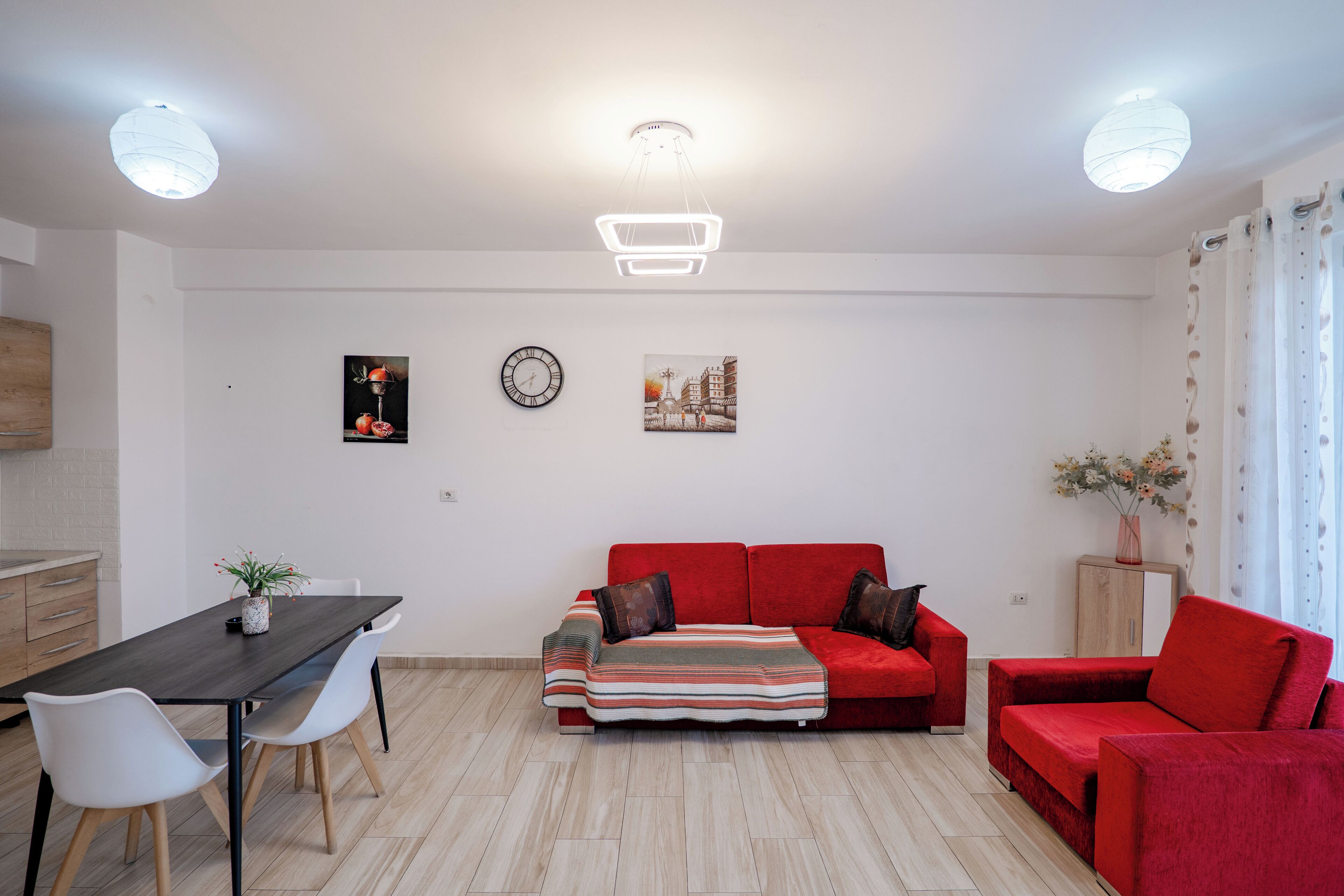Una sala de estar moderna con una mesa de comedor, dos sofás, un sofá rojo, un reloj y un cuadro en la pared.