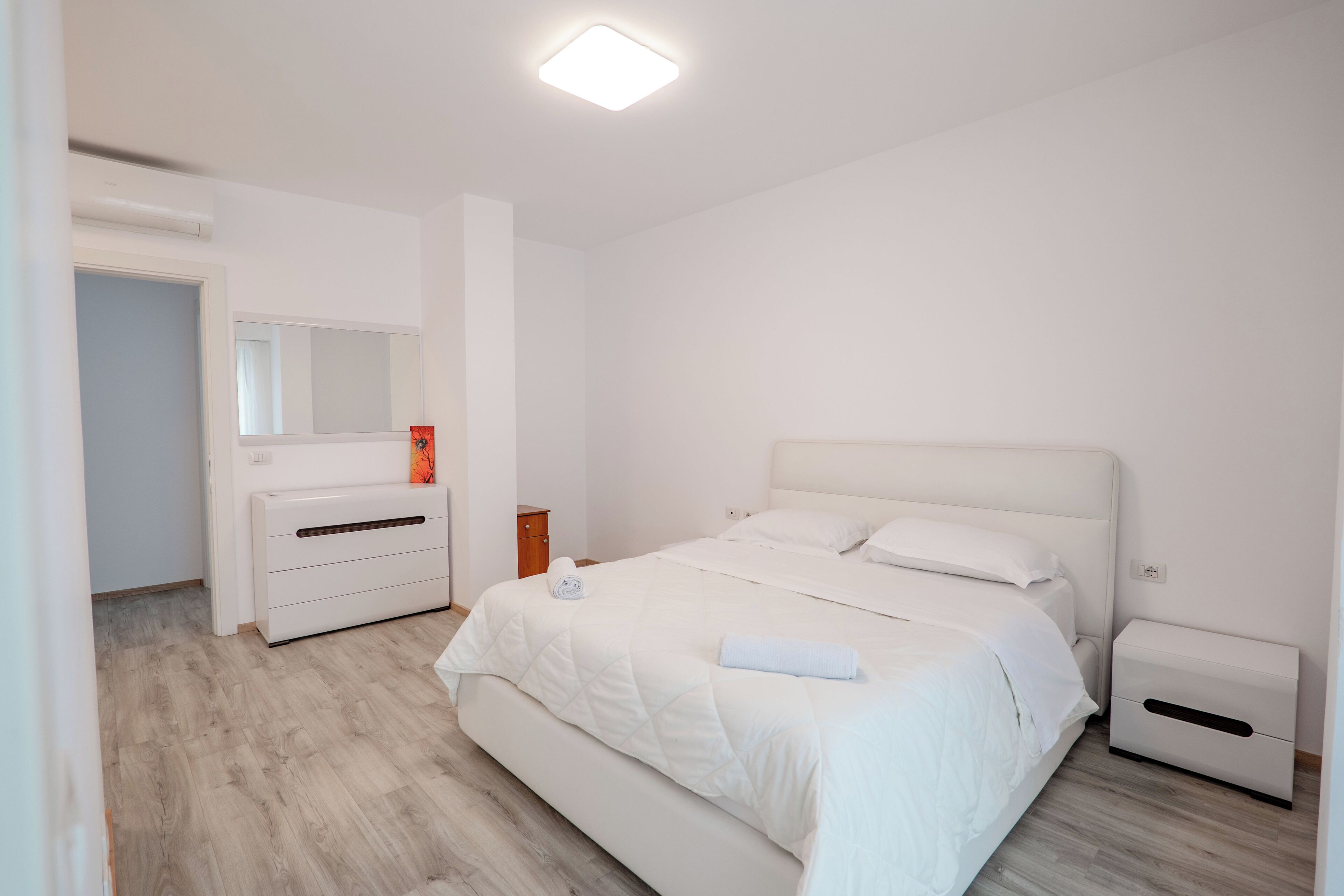 A bedroom with a bed, bedside tables, a dresser, a mirror, and a ceiling light.