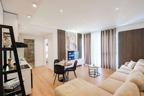 Un salon moderne comprenant un canapé, une table à manger, des chaises, un téléviseur et un coin cuisine.