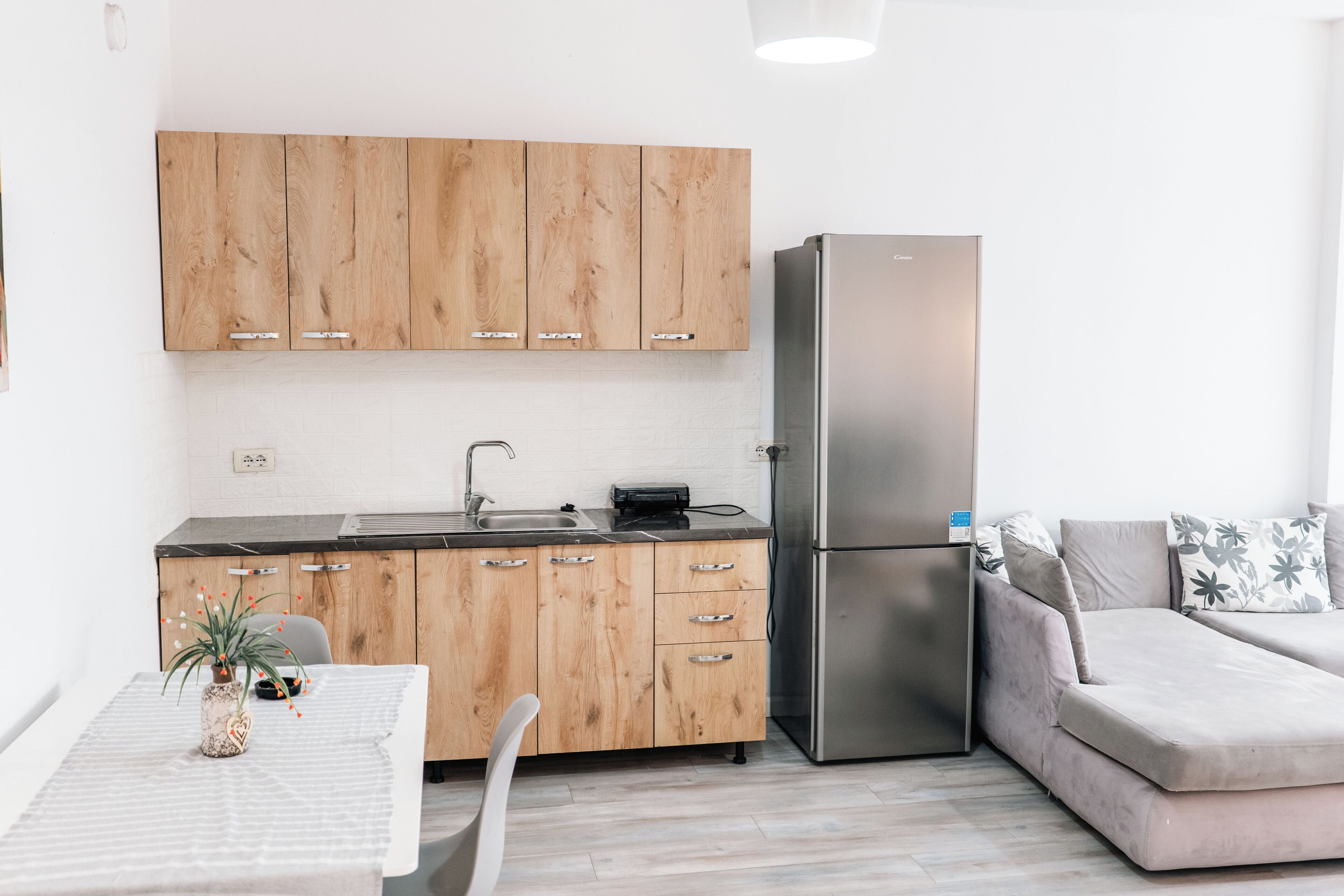 Una cocina moderna con armarios de madera, un refrigerador de acero inoxidable, una mesa de comedor con una planta y un sofá.