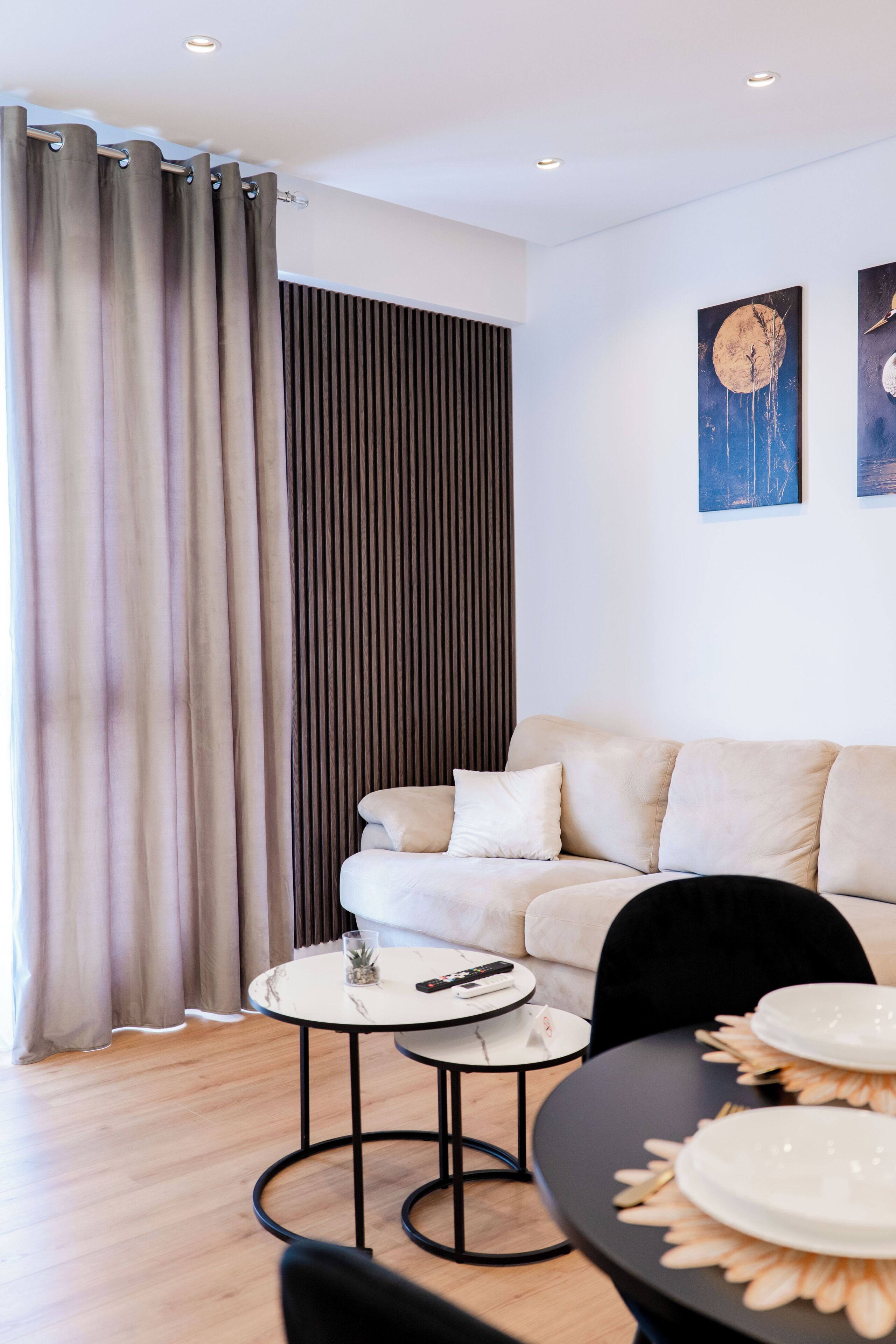 A modern living room with a sofa, two side tables, and a dining area with plates and cutlery.