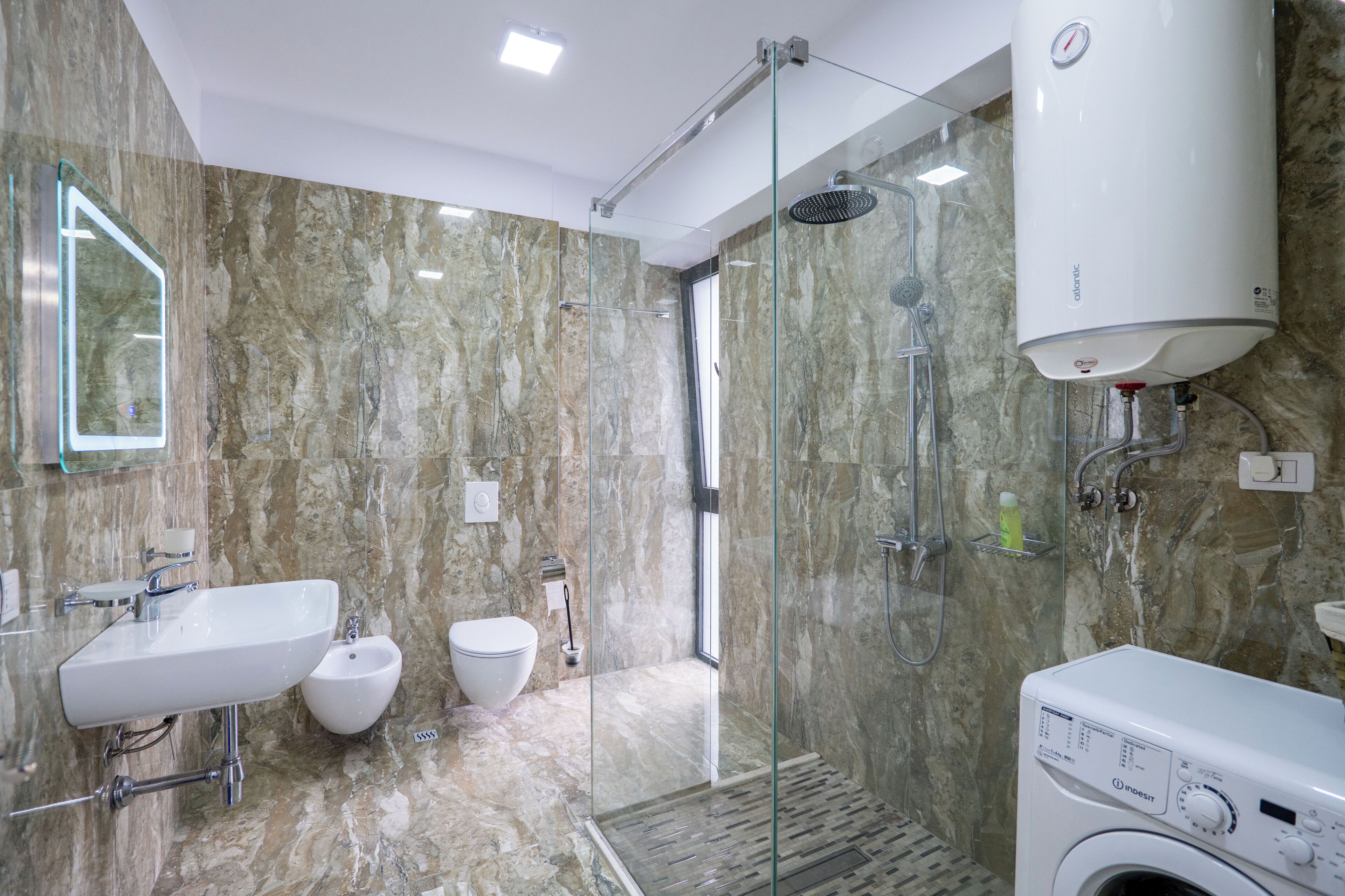 A modern bathroom with a glass-enclosed shower, a built-in sink, a bidet, and a washing machine.