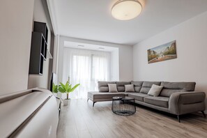 Un salon moderne avec un canapé d’angle, une table basse, une plante en pot et un tableau accroché au mur.