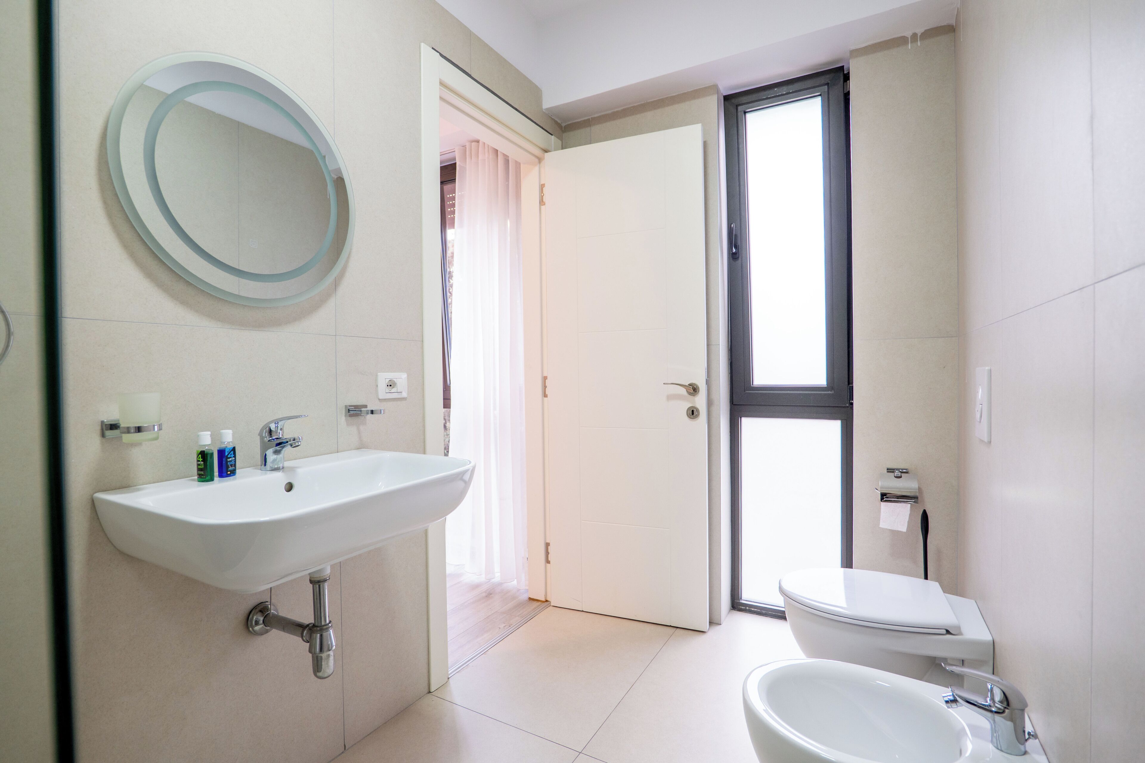Une salle de bain équipée d’un lavabo, d’un miroir, de toilettes et d’une porte donnant sur une autre pièce.