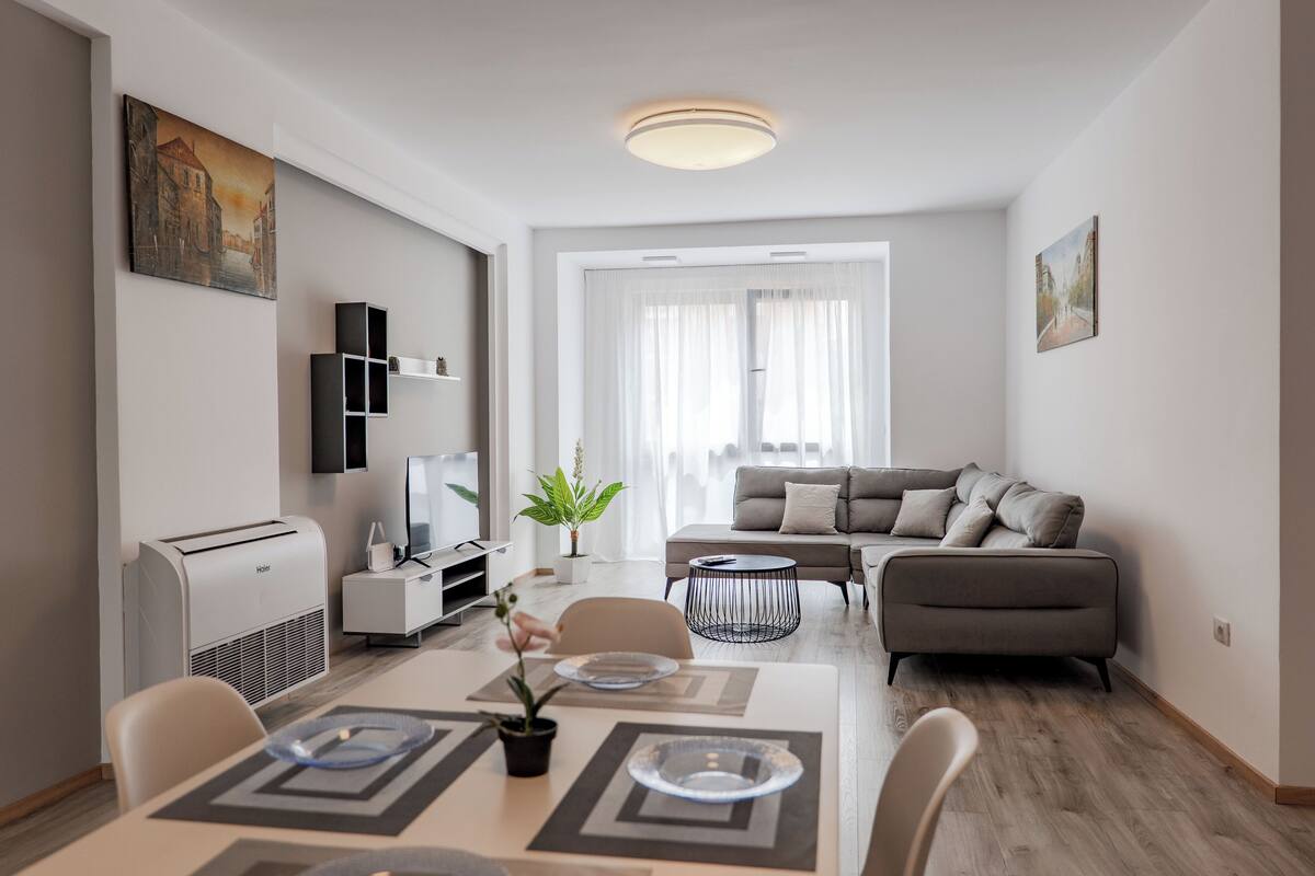 Un salon moderne avec un canapé, une table à manger et des chaises, un téléviseur et un luminaire au plafond.