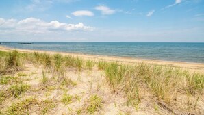 Een strand met zand en gras op de voorgrond, en een rustige zee op de achtergrond.