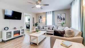 Een moderne woonkamer met een flatscreen televisie, een plafondventilator, een bank, een salontafel en een open haard.