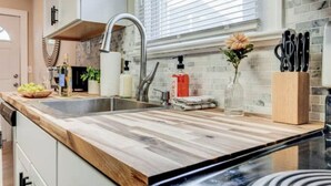 Een moderne keuken met een houten aanrecht, een roestvrijstalen spoelbak en een raam met zonwering.