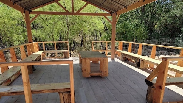 A wooden deck with benches and a table, surrounded by a metal fence and trees. - Vigilante Inn Covered Wagon (Tombstone)